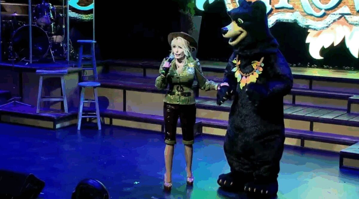 Dolly Parton poses with a black bear mascot while announcing a new roller coaster coming to Dollywood in spring 2023 called Big Bear Mountain.