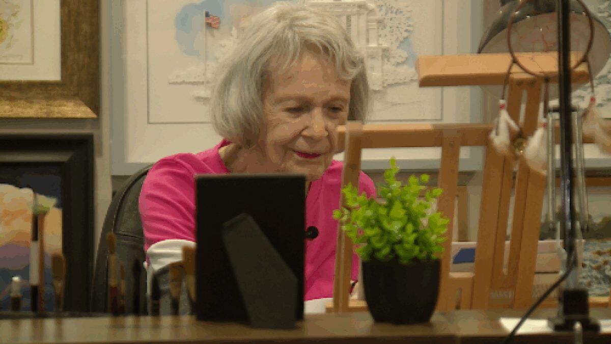 Judy Manning finishes a painting in her den art studio surrounded by her late husband's artwork who designed the Royals crown logo while working at Hallmark Cards.