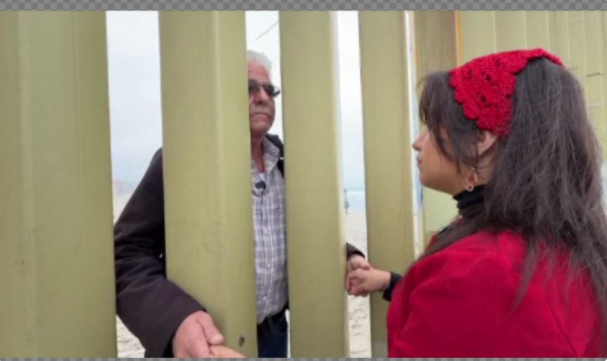 They hold hands through steel poles at the US-Mexico border